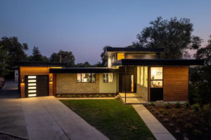 A modern home showcasing one of the best ROI home upgrades with a sleek black metal and stone exterior, expansive windows, and a beautifully landscaped front yard. The sunset enhances the curb appeal, highlighting the high-return investment in contemporary design, energy-efficient materials, and outdoor enhancements.